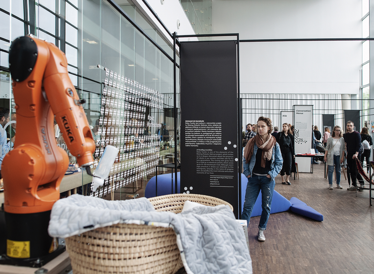 Lady looking at an orange arm of a big industrial robot